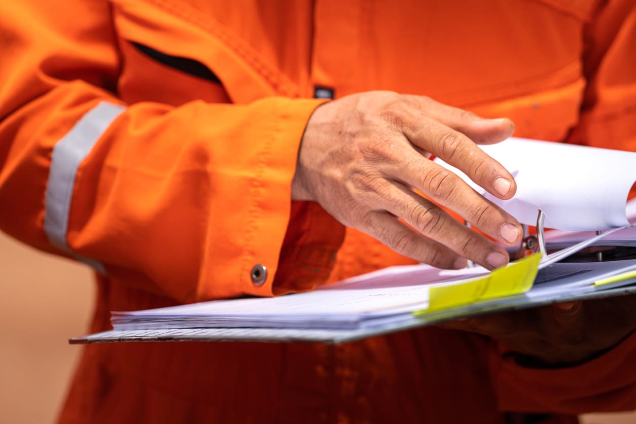 A worker in orange coverall uniform is opening documents to make a discussion on working procedure, safety audit in operation action photo.